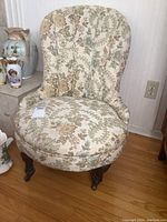 Full view of one floral tufted slipper chair with wooden legs on a hardwood floor