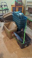 Stacked blue-green large Rubbermaid Roughneck storage totes with lids, tan medium totes to side, and dark gray small totes in front.