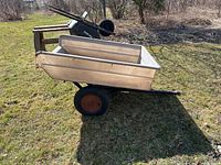 Side view of utility garden trailer with plastic beige dump bed and black metal frame, showing overall shape and structure.