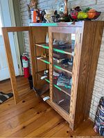 Front angled view of wood bookcase showing doors, shelves, and contents inside while positioned against a wall with wood floor beneath.