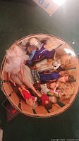 Wide top-down view of a wooden basket filled with approximately 16 dolls in various outfits and poses.