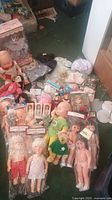 Full top-down view of assorted dolls, doll clothing, accessories, and shoes spread on floor