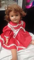 Front view of ideal doll showing face, curly brown hair, and red dress with white lace.