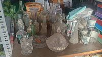 Overview of assorted glass jars, bottles, glasses, vases, and candle holders on a wooden table.