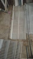 Top-down view of bundled white metal shelving panels laid on the floor showing vertical and horizontal bars.