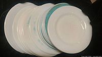 Photo showing a stack of mostly white milk glass plates with some faded teal accents, showing overall condition and plate details.