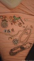 Photo showing a variety of vintage costume jewelry items including earrings, brooches, clips, charms, and necklaces spread out on a peach-colored fabric.