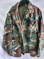 Front view of the US Air Force camouflage jacket showing patches, button-up front, pockets, collar, and epaulets.