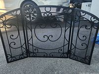 Front view of the black cast iron fireplace screen showing detailed scroll patterns on three panels.