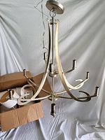 Chandelier photographed showing metal curved arms and sockets, light covers in box to left.
