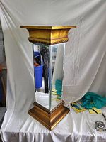 Front and side view of the mirrored pedestal stand showing the wooden framed base and top with mirrored panels on the sides.