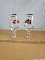 Two Stella Artois chalice beer glasses showing gold rim and logo on clear glass with stems.