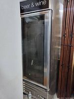 Photo of the front glass door with stainless steel frame, 'beer & wine' label at top, and the cooler unit exterior.
