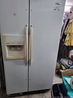 Front view of white Whirlpool side by side fridge freezer with water and ice dispenser on freezer door, showing vertical handles and marks on surface.