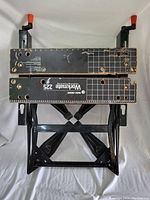 Top view of the portable Workmate 225 workbench showing black work surface with printed white grid, holes, and orange clamp handles