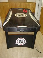 Front view of black NHL air hockey table showing playing surface, puck, pushers, and NHL logo on table base.