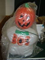 Halloween blow mold decoration light featuring a smiling pumpkin head and the word 'BOO' on the white body under plastic wrapping.