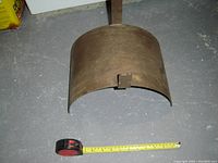 Metal garden hose bracket placed on concrete floor with a measuring tape showing approximately 8 inches width.