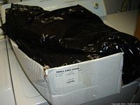 Black plastic cart covers inside a worn cardboard box, partially opened showing one cover.