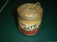 Sealed cylindrical ball of natural brown jute twine with paper label showing brand and product description.
