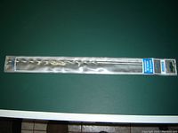 Full view of the masonry bit packaged in clear plastic showing the spiral metal bit extending the full length of the package.