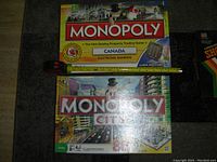 Photo of two Monopoly board games stacked, Monopoly Canada Electronic Banking on top, Monopoly City underneath