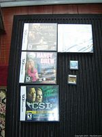 Top view photo showing three Nintendo DS game cases (Rooms, Nancy Drew: The Model Mysteries, CSI Deadly Intent) and three DS game cartridges (two loose and one sealed) on a wooden floor.