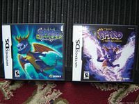 Photo showing two Nintendo DS game cases: Spyro - Shadow Legacy and Spyro - A New Beginning, positioned side by side on fabric background.