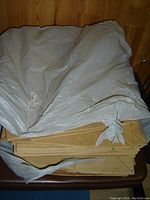 Photo of stacks of brown flat paper leaf bags bundled together with paper ties. A white plastic bag is placed on top of the stacks. The bags appear new and unused.