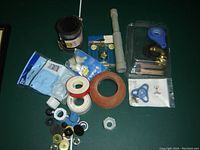 Photo showing assorted plumbing parts including valves, washers, Teflon tape, pipe fittings, and connectors spread out on a surface.