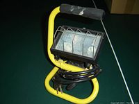 Quartz worklight on yellow metal stand with black foam handle and plug-in cord wrapped around base.