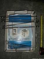 Shish kebab set including multiple metal skewers with loop handles, a rectangular frame and instruction sheet displayed in box with measuring tape.