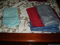 Folded assorted table covers on a floral bedsheet showing various colors and patterns.