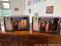 Two boxed sets of canvas Moscow Mule mugs, each box holds 2 mugs. One box unopened, the other box opened showing mugs inside.