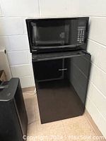 Black Hisense bar fridge with microwave on top, showing front and some side angle.