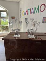 Photo showing two clear crystal 5-arm candlesticks on a dark polished surface with a bright interior background.