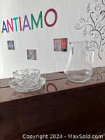 Photo showing clear glass pitcher, a bowl with petal-like pattern, and a dish, all made of clear glass on a wooden surface.