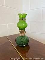 Green glass oil lamp with a rounded base and decorative metal fitting at the middle and top.