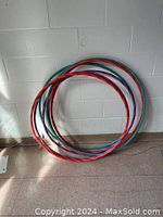 Photo of a group of hoola hoops leaning against a white wall on floor, showing multiple colors.