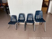 Four blue plastic kids chairs in different sizes, lined up side by side on a tiled floor with a white cinder block wall behind them.
