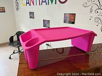Pink plastic lap desk shown standing on a wooden dining table with visible dual cup holders and storage area.