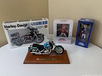 Photo of all four items: Honda model motorbike on wooden base, boxed Harley-Davidson Electra Glide model kit, and two boxed sports bobbleheads (Aaron Sanchez and Marco Estrada).