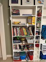 Full front view of the white bookcase filled with various books, board games, and other items.