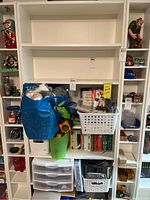 Front view of the white bookcase with shelves and some items stored on the lower shelves and around it (items not included).