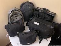 Photo showing all 7 bags arranged on a round table including backpacks and briefcase.