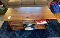 Full frontal view of wood coffee table showing surface top and open shelving beneath with items removed except for some boxes and containers for reference.