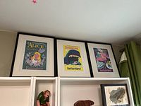 Three framed Walt Disney World Fantasyland themed prints displayed on top of a shelf, each framed in black with white mats.