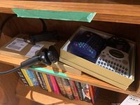 Wide shot showing two Dynamo label makers in box, clamp-on phone holder in foreground, and unopened keyboard box beneath shelf