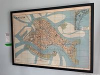 Framed map of Venice hanging on the wall, showing detailed canals and layout with a black wooden frame and glass front.