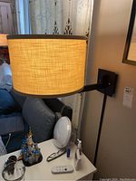 Light sconce with fabric shade illuminated, mounted on wall above couch. Shows size and style of the fabric shade.